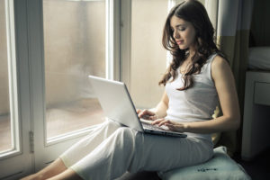 窓際でパソコンを触る女性の画像